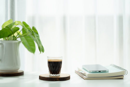 Coffee in a glass cup and philodendron and phone arranged on white table