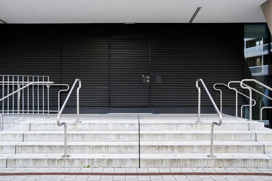 Wide modern staircase with symmetrical metal handrails leading toward a dark building entrance and forming a strong geometric composition