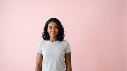 Obraz premium A smiling young woman with dark wavy hair wearing a grey t-shirt against a soft pink background