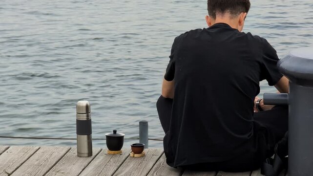 Man sitting on a dock during lunch break, enjoying peaceful moments by the water. Casual and calm atmosphere reflecting relaxation and a brief escape from the workday routine.