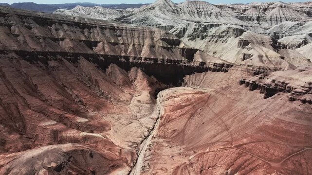 Aerial view of eroded badlands canyon with layered red and pink sedimentary rock formations and striped geological patterns in Aktau Mountains, Altyn Emel National Park, Kazakhstan