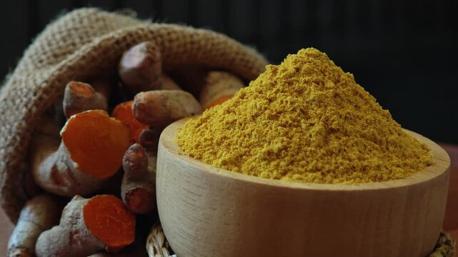 Turmeric powder in a wooden bowl with turmeric rhizomes.
