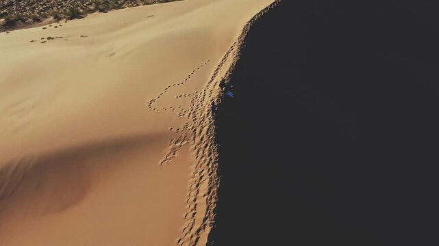 Aerial view of a massive sand dune ridge with sharp crest casting dramatic shadow over sparse desert vegetation - Singing Dune, Altyn Emel National Park, Kazakhstan