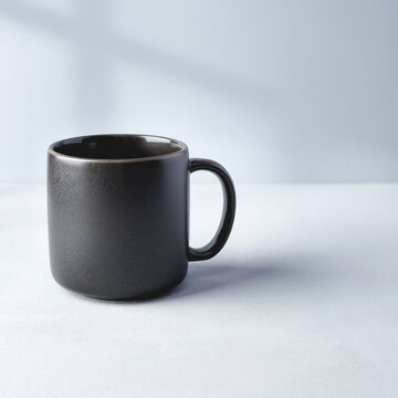 A simple, modern, dark gray ceramic mug with a handle sits on a white surface with soft shadows.