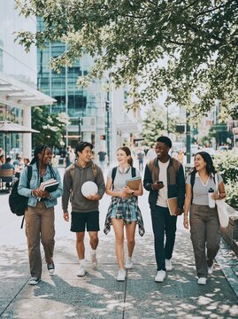 Diverse group of college students walking on a city sidewalk smiling with books and backpacks