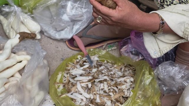 Local vendor peeling fresh cassava root at a traditional market in Vietnam