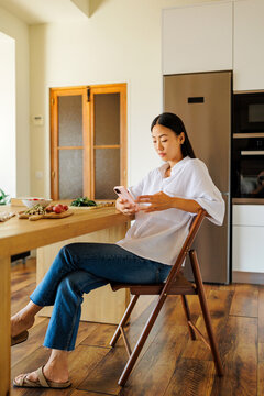Woman using smartphone sitting kitchen table