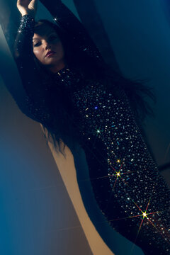 Woman in crystal embellished gown under starburst lights, night party glamour concept.