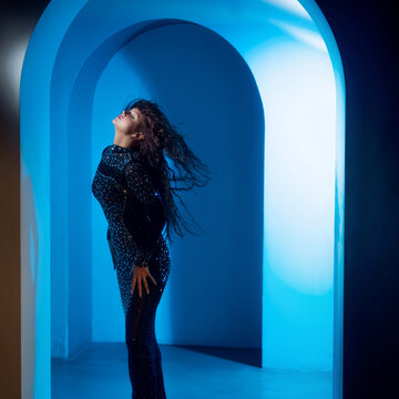Dreamcore fashion portrait, woman with flying hair in a glowing blue arch, surreal aesthetic.