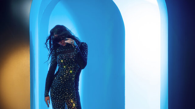 Woman hiding face behind flying hair in a blue arch, mystery and anonymity concept.