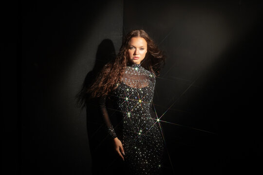 Fashion editorial portrait, woman in a rhinestone gown at a dark wall, model portfolio shot.