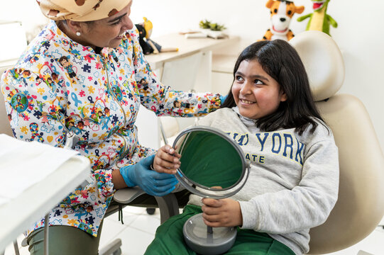 Girl smiling at dentist holding mirror in pediatric clinic