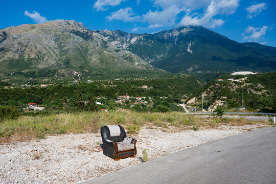 Lonely armchair beside mountain road under blue sky, real lifestyle countryside illustration of solitude and nature in Albania.