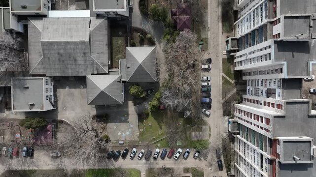 Drone aerial top-down view moves across apartment buildings, courtyards and parked cars in a residential district. Urban housing and neighborhood infrastructure