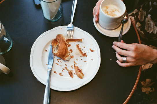Person Enjoys Pastry and Coffee at a Cafe Table in the Morning