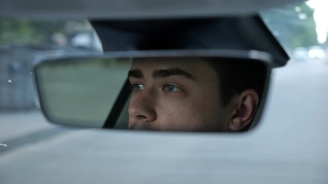 Male eyes of driver reflecting in rearview mirror while riding modern electric car. Young man looking concentrated to urban road during operating motor vehicle capturing focused gaze during city trip