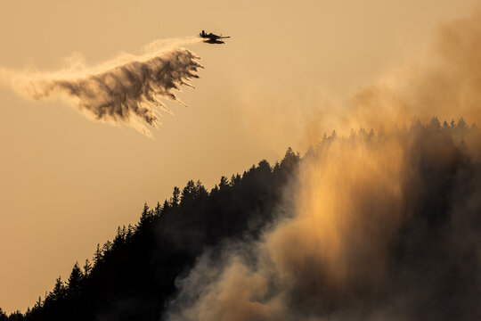 Airplane drops water on a wildfire from above.