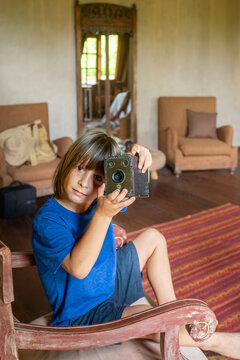Little Boy with Long Hair Holding Vintage Box Camera in Rustic Room