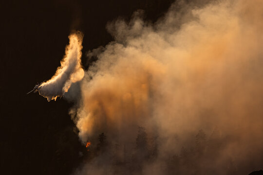 Airplane drops water on a wildfire from above.