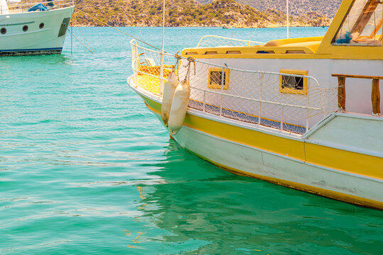 Bow of a yellow and white traditional tour boat floats on calm turquoise water, Turkish coastal vessel.