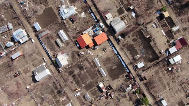 Aerial view reveals rural settlement beside vast farmland. Sunlit houses and buildings dot the earthy landscape. Roads divide the village from open agricultural fields. , so no emotions to report