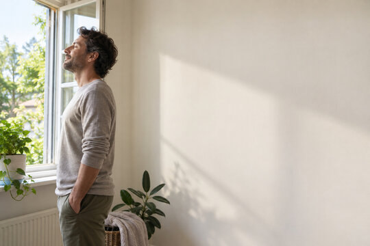 Calm man practicing slow breathing beside a bright open window.