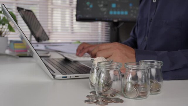 Businessman calculating and allocating money into jars with coins on office desk, concept of financial planning, saving, budget management, investment, and wealth management.