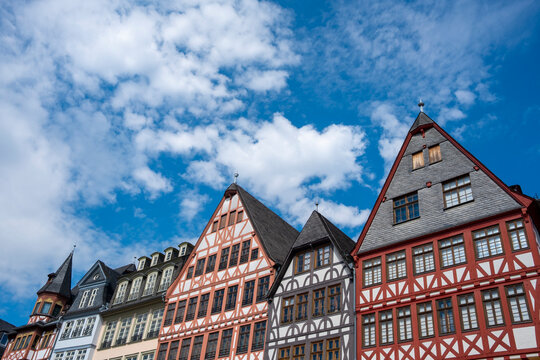 Historic architecture at R&ouml;merberg in Frankfurt Germany shows a row of half-timbered houses with colorful facades beneath dramatic clouds and blue sky