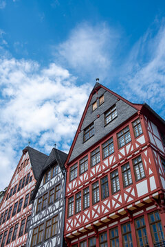 Historic half-timbered houses at R&ouml;merberg in Frankfurt Germany rise vertically with colorful facades and gabled roofs against a bright cloudy sky