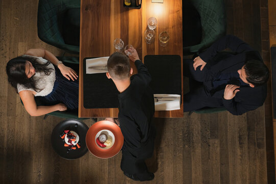 Waiter presents dessert to couple during fine dining experience in restaurant. They share a table and enjoy gourmet food.