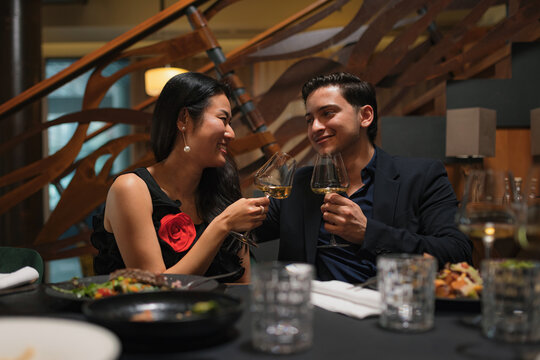 A happy couple celebrates with a toast at a restaurant during a special dinner. They enjoy each others company over food and wine.