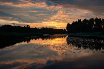 Obraz premium A magical landscape featuring a beautiful sunset or sunrise over a pond or lake on a summer evening, with a cloudy sky in the background, reflections on the water