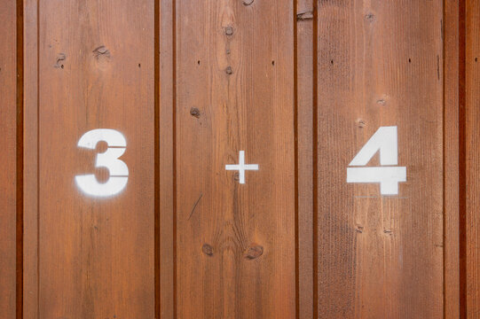 Natural timber background featuring painted white numbers three and four with plus sign
