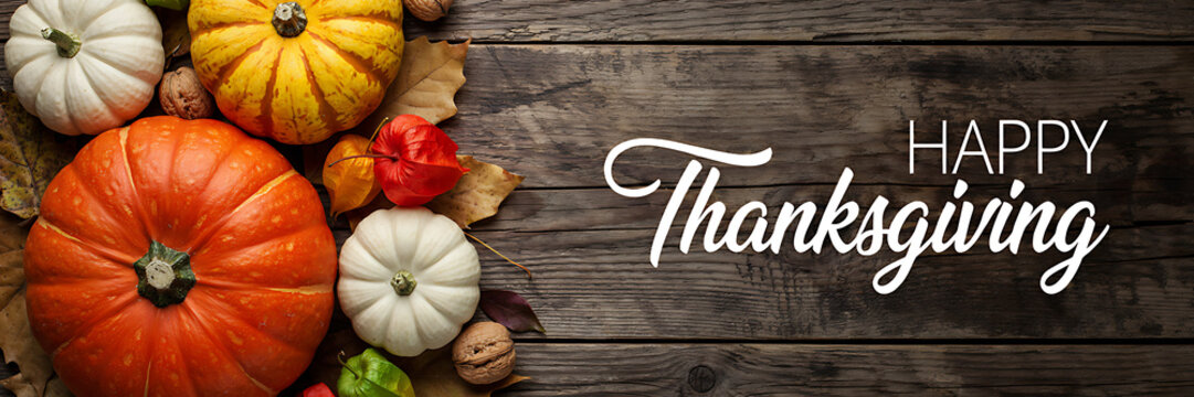 Happy thanksgiving greeting with pumpkins, autumn leaves, and walnuts on a rustic dark wooden background, for seasonal holiday celebration