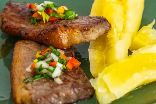 Carne de sol, a traditional northeastern Brazilian dish of salted sun-dried beef served with boiled cassava, fresh onion and bell pepper vinaigrette, chili pepper sauce and acerola juice.