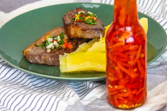 Carne de sol, a traditional northeastern Brazilian dish of salted sun-dried beef served with boiled cassava, fresh onion and bell pepper vinaigrette, chili pepper sauce and acerola juice.