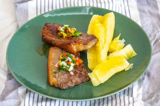 Carne de sol, a traditional northeastern Brazilian dish of salted sun-dried beef served with boiled cassava, fresh onion and bell pepper vinaigrette, chili pepper sauce and acerola juice.