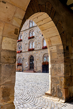 A view through a historic stone archway of a building with window boxes and cobblestones; the arches of the historic town hall in Alsfeld