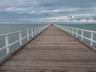 Fototapeta premium Long wooden pier with white railings extending into calm ocean in Australia