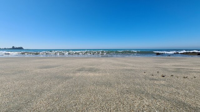 Tranquil coastal vista featuring a wide expanse of sun-kissed sand meeting the gentle ebb and flow of the ocean beneath a boundless azure heaven, inviting serenity