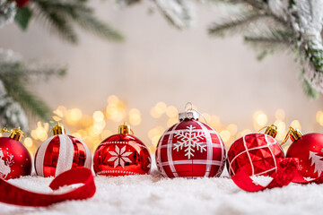 Naklejka premium A Christmas background featuring a row of red baubles decorated with snowflakes, reindeer, and pine motifs beneath frosted branches on snow, softly lit by warm twinkling lights with copy space.
