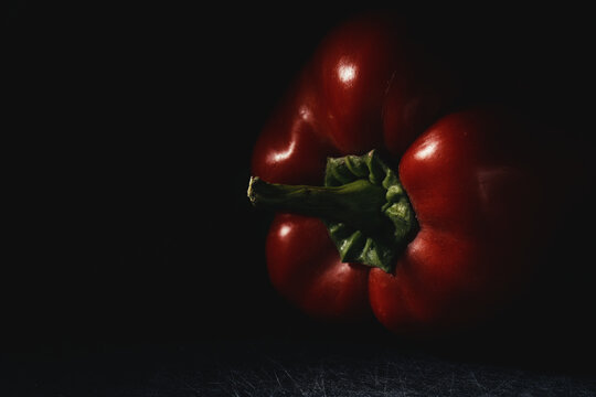 Close-up of ripe red bell pepper with vibrant green stem in moody lighting on dark background. Fresh raw vegetable for organic recipes, culinary menus, nutrition, and healthy eating.