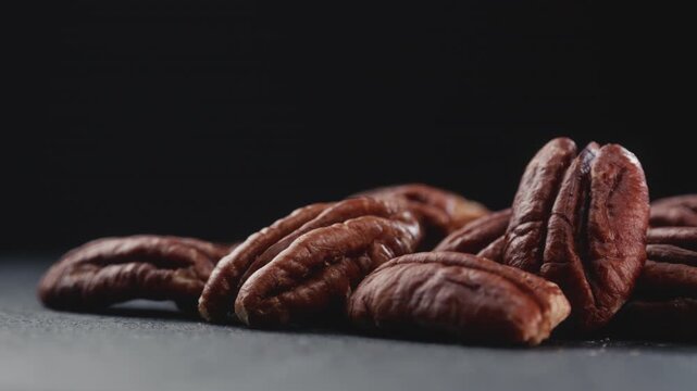 Macro shot of fresh premium pecan nuts with selective focus, sliding camera shot on dark background with artistic lighting. Perfect for healthy eating, gourmet food, culinary, and dietary content.