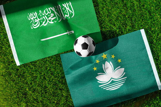 Saudi Arabia vs. Macau football match. National flags on green grass with soccer ball in the middle. Football background for international match.