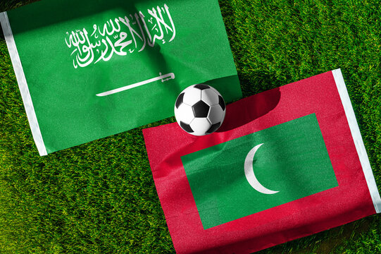 Saudi Arabia vs. Maldives football match. National flags on green grass with soccer ball in the middle. Football background for international match.