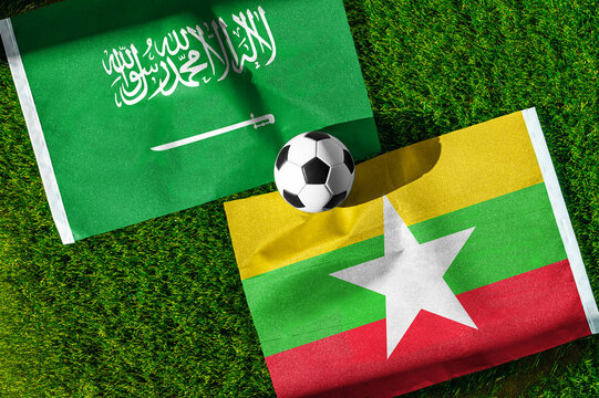 Saudi Arabia vs. Myanmar football match. National flags on green grass with soccer ball in the middle. Football background for international match.