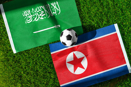 Saudi Arabia vs. North Korea football match. National flags on green grass with soccer ball in the middle. Football background for international match.