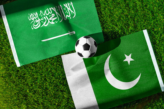 Saudi Arabia vs. Pakistan football match. National flags on green grass with soccer ball in the middle. Football background for international match.