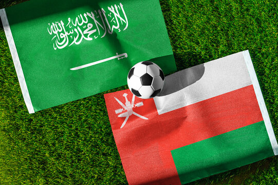 Saudi Arabia vs. Oman football match. National flags on green grass with soccer ball in the middle. Football background for international match.