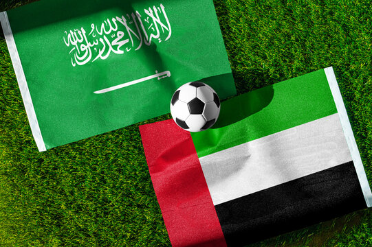 Saudi Arabia vs. United Arab Emirates football match. National flags on green grass with soccer ball in the middle. Football background for international match.